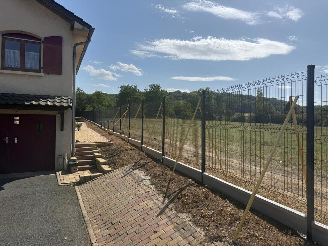 Chantier de clôture rigide en cours le long d'une allée pavée, camion de l'artisan sur le terrain